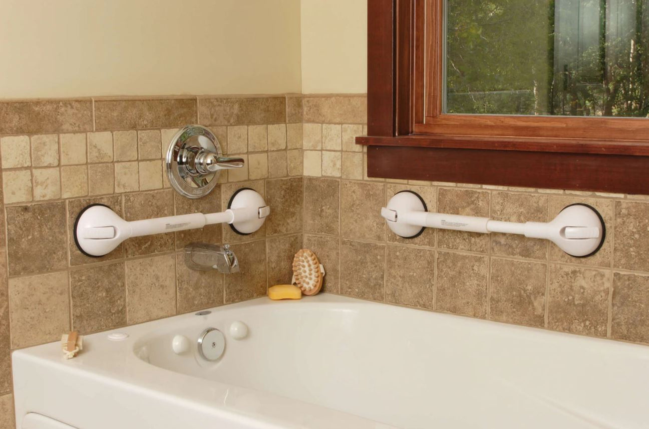 A bathtub with tan tile walls, featuring two white suction grab bars, a soap bar, a bath brush, and a window above the bathtub.