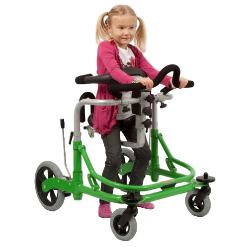 A young girl with blonde pigtails sits on a green and silver mobility walker or tricycle wheelchair, wearing a pink cardigan and dark pants, isolated on a white background.